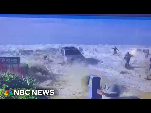 People flee from big waves as they break over a sea wall